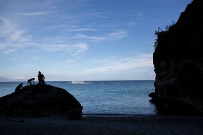 People on rock by sea against sky