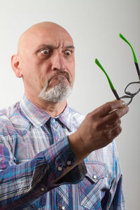 Close-up of angry senior man holding eyeglasses against white background