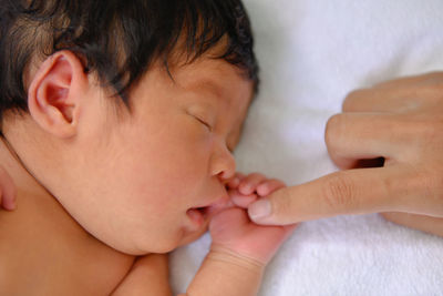 Cropped finger of woman touching baby girl hand on bed