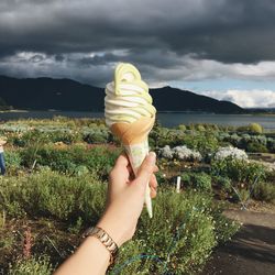Midsection of woman holding ice cream by plants against sky