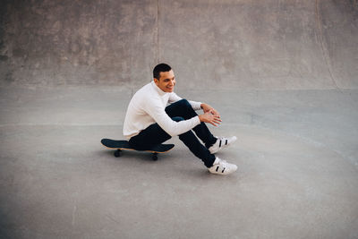 Full length of smiling man sitting on skateboard at park