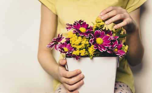 Midsection of woman holding flowers against wall