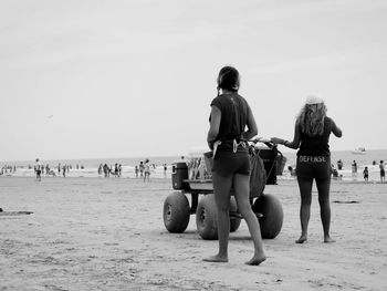 Women with cart walking at beach against sky