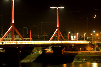 Illuminated bridge over river against sky at night