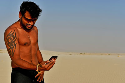 Young man using mobile phone at beach against clear sky