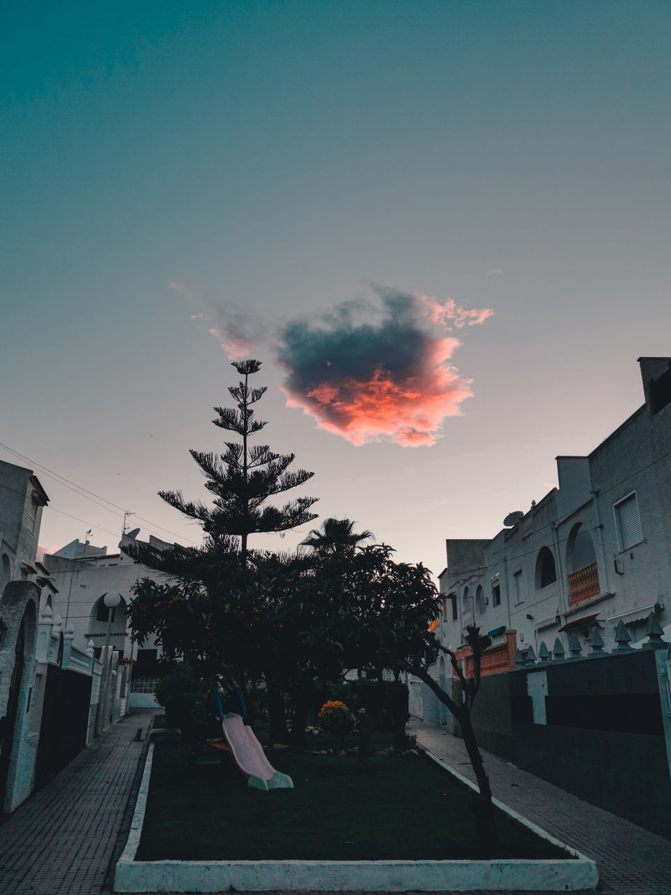 STREET AMIDST BUILDINGS AGAINST SKY AT SUNSET