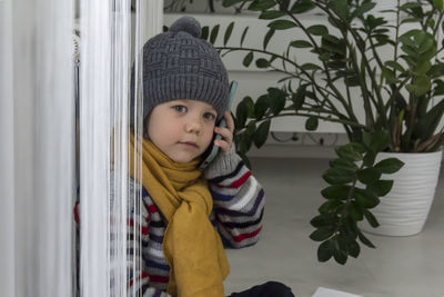 A small child with a yellow scarf near the radiator speaks on the phone.  energy crisis concept