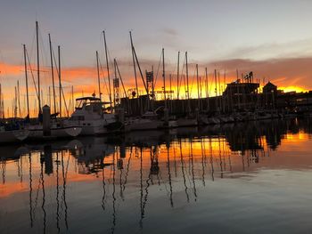 Sailboats moored at harbor against sky during sunset