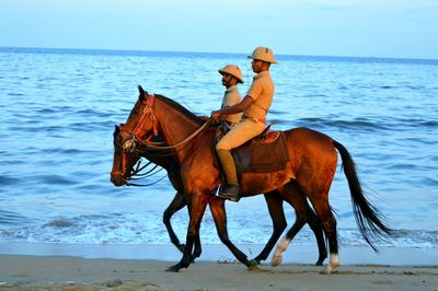 Side view of male police officers riding horses at beach