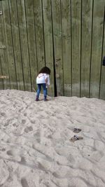 Rear view of girl peeping in wooden door while standing on sand at beach
