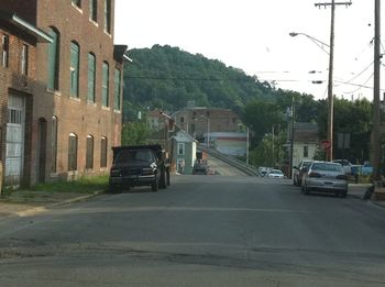 Cars on road by buildings in city against sky