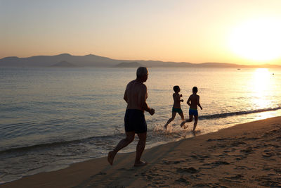 People standing on beach against sky during sunset