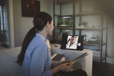 Side view of architect with fabric swatch talking through laptop on video conference while working at home