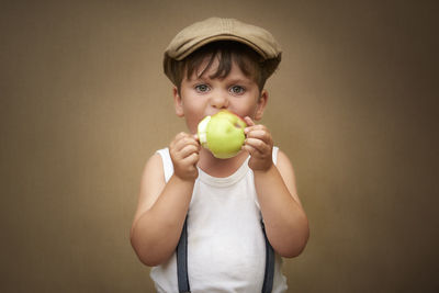 Close-up portrait of boy eating granny smith apple against wall