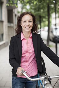 Portrait of happy businesswoman with bicycle standing on sidewalk