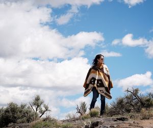 Woman wrapped in blanket standing on field against sky