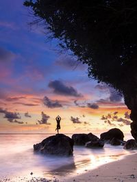 Silhouette young man standing on beach against sky during sunset