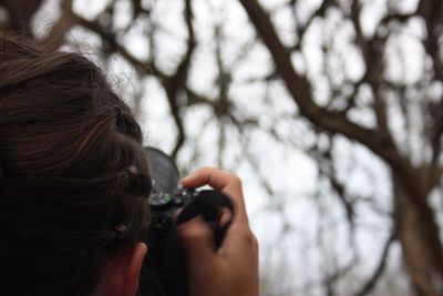 Cropped image of woman photographing against bare trees