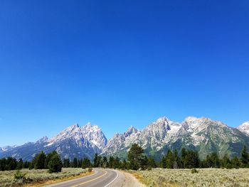 Road by snowcapped mountains against clear blue sky