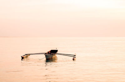 Man rowing boat in sea against sky during sunset