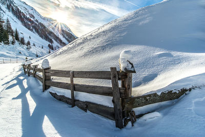 Fence in the fresh snow against the mountains and the sun