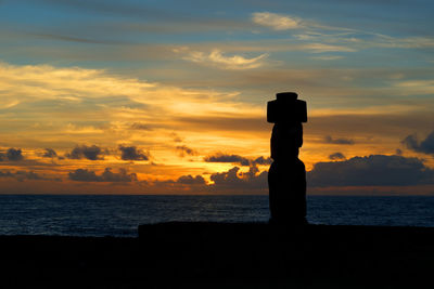 Silhouette cross on beach against sky during sunset