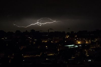 Lightning over illuminated cityscape against sky at night