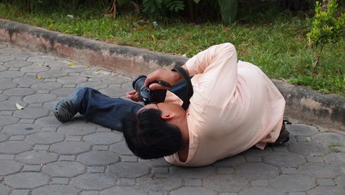 Man photographing while lying on footpath