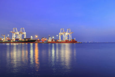 Illuminated commercial dock by sea against sky at night