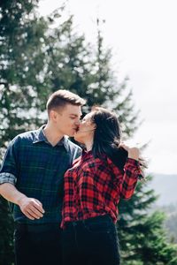 Young couple kissing while standing in forest during sunny day