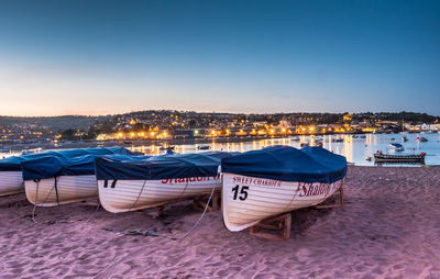 Boats moored on beach against clear sky during sunset