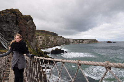 Woman standing on footbridge by sea against sky