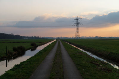 Road amidst field against sky during sunset