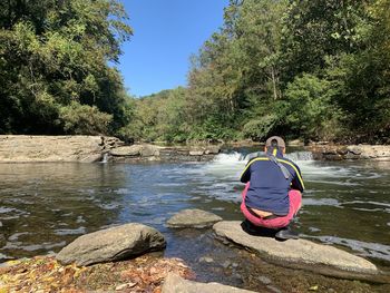 Rear view of man crouching on rock in lake