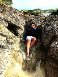 Full length of young man lying amidst rocks at beach against sky