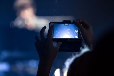 Cropped hands photographing illuminated lights at night