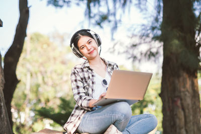 Young woman using phone while sitting on tree trunk