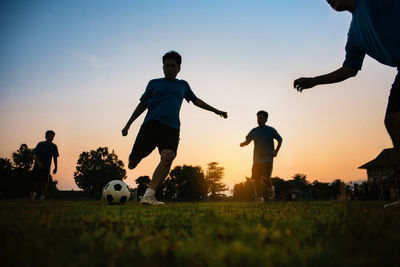 People playing soccer ball on field against sky during sunset