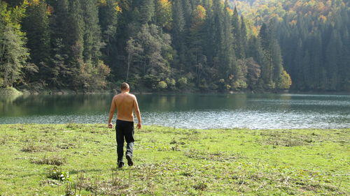 Rear view of man standing by lake against trees