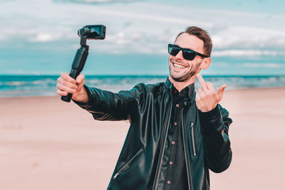 Smiling man gesturing while vlogging at beach