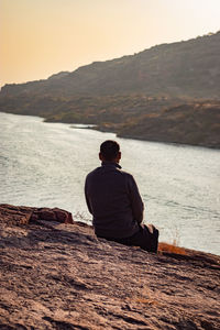 Isolated man sitting at mountain top with lake view backbit shot from flat angle