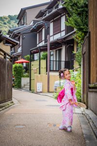 Portrait of cute girl standing on street by buildings in city