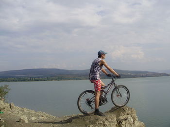 Man riding bicycle on shore against sky