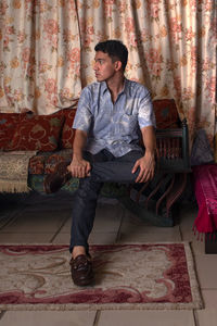 Full length of young mixed race man sitting on vintage sofa at home