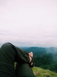 Low section of man relaxing on mountain against sky