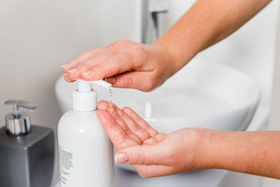 Crop anonymous female pressing dispenser with sanitizer gel placed on counter near sink