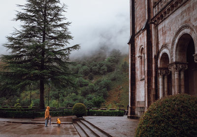 View of a child and an adult playing under the rain near a big monument 