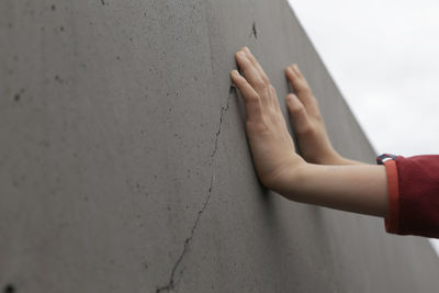 Cropped image of person leaning hands on concrete wall against sky