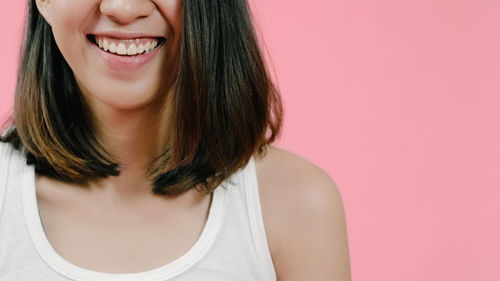 Close-up portrait of a smiling young woman over pink background