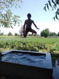 Man jumping by lake against sky